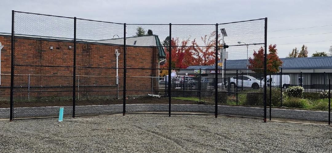 Chain-link fence around a gravel lot beside a brick building under a cloudy sky