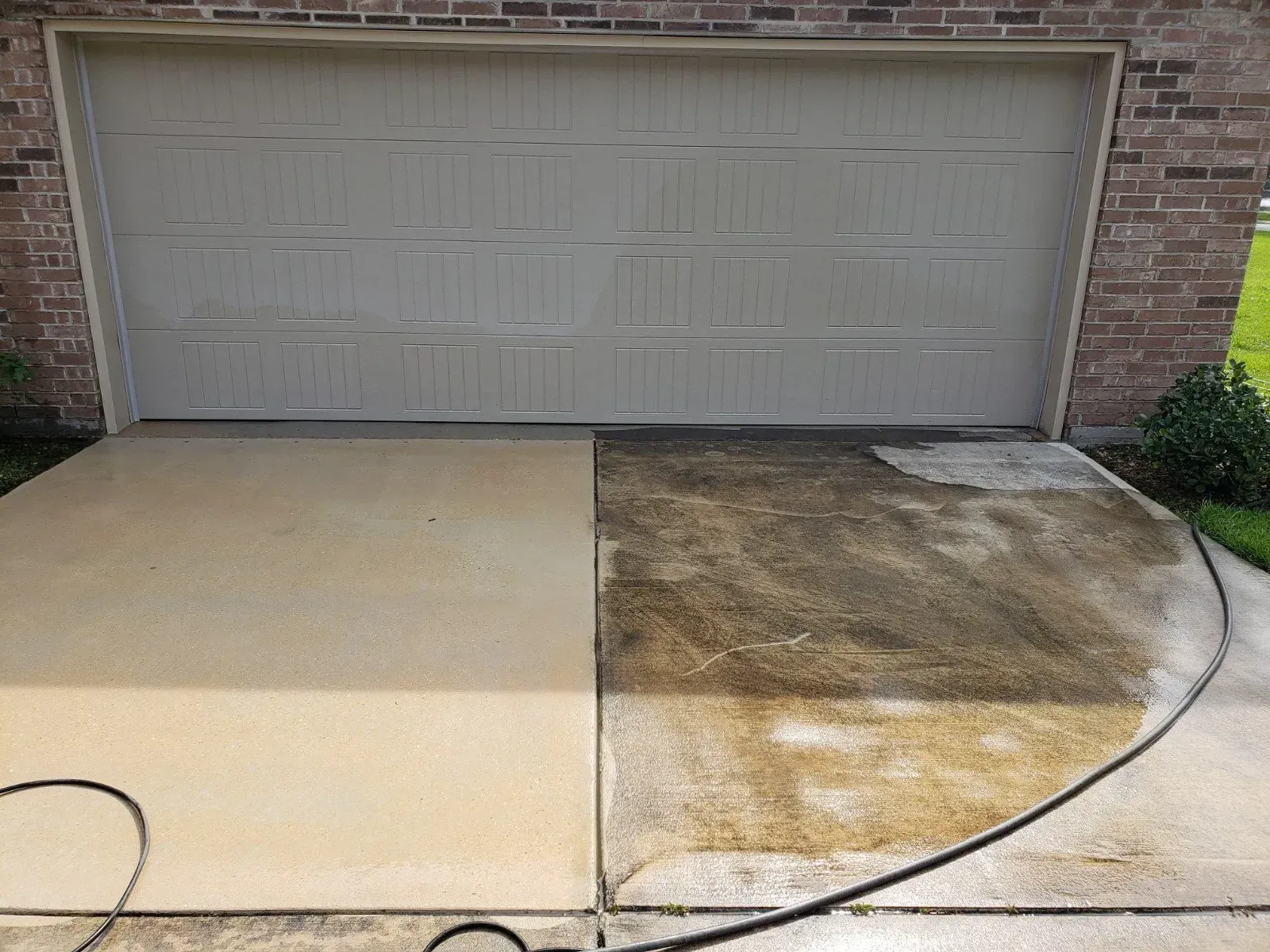 A driveway in front of a garage, showing the stark contrast between a clean, light-colored side and a dirty, dark side.