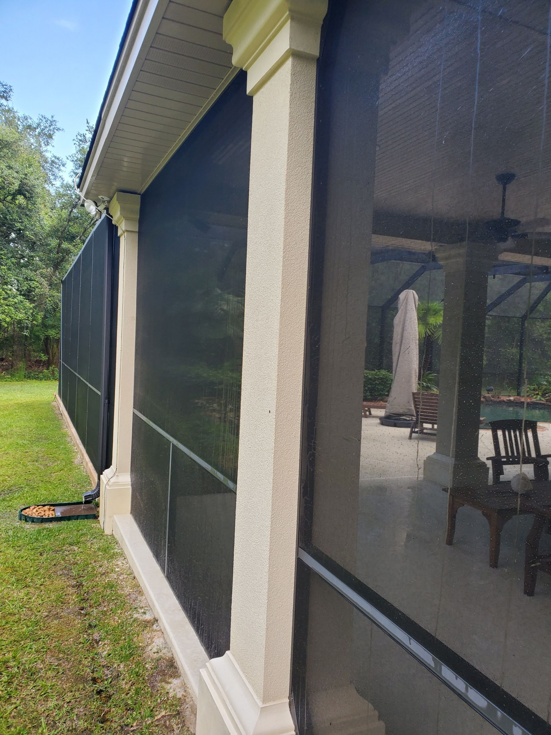 A low-angle view of a beige stucco column and black screen enclosure surrounding a patio and swimming pool.