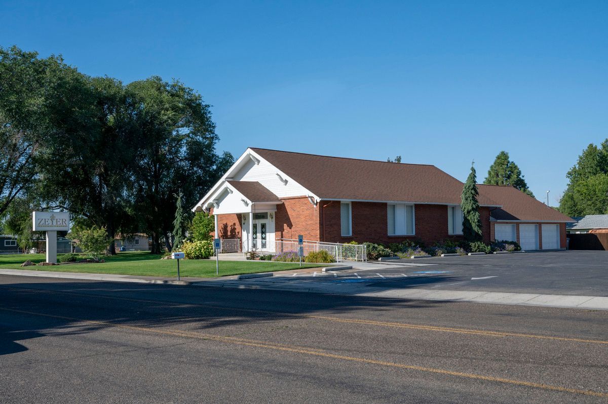 Small red brick building with white trim beside a parking lot and trees on a sunny day
