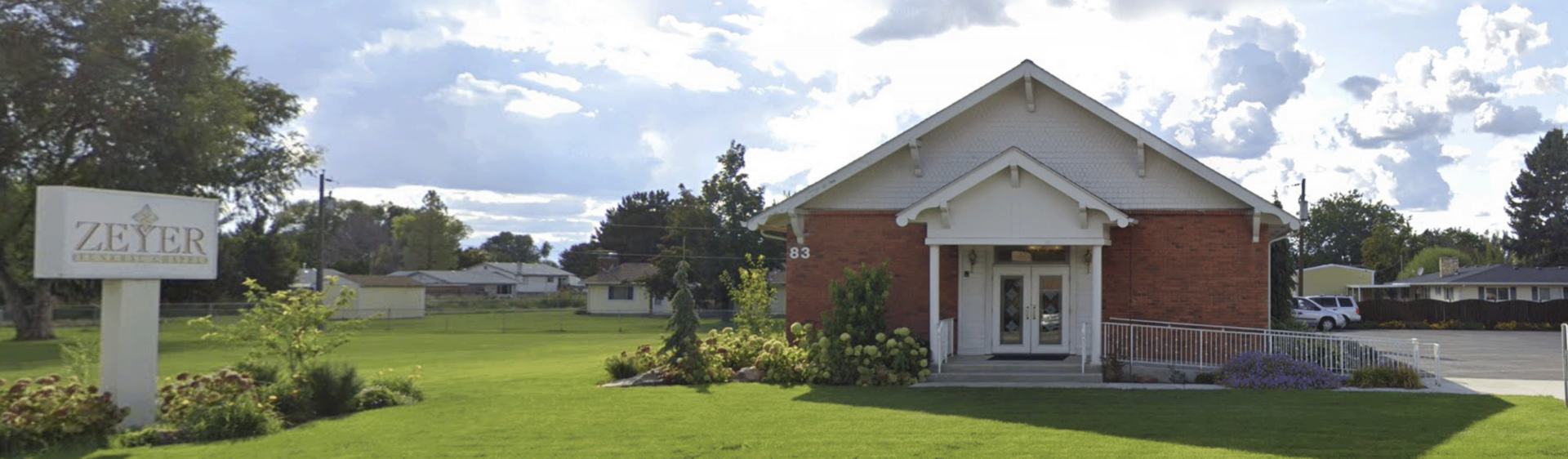 Brick church with white columns and steeple on a grassy lawn under a cloudy sky