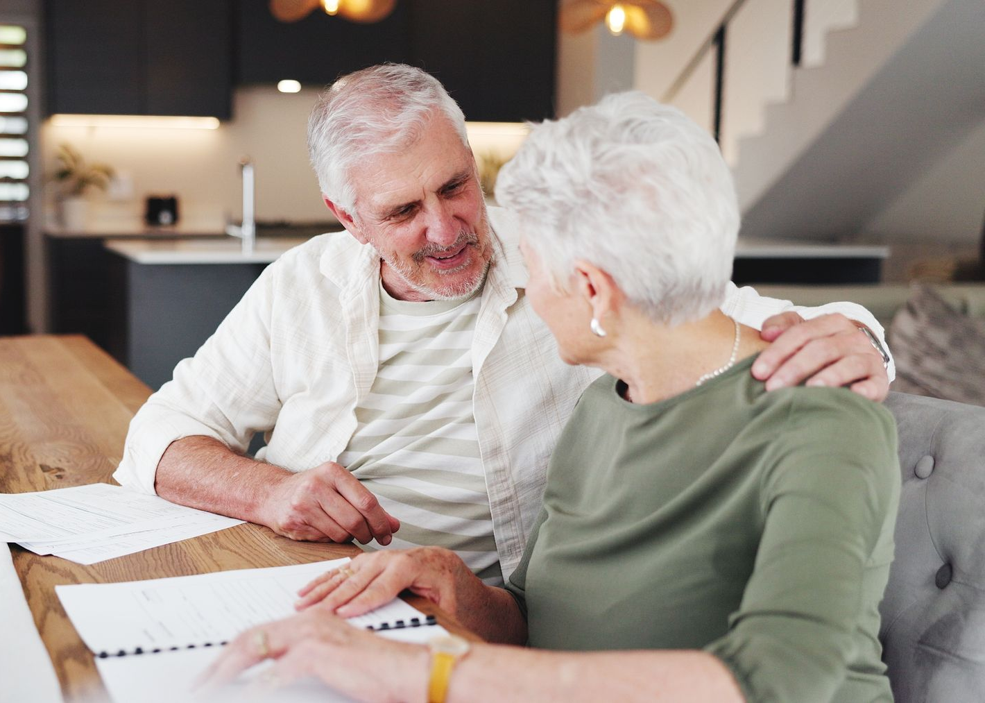Two older adults reviewing documents together at a table in a bright home interior