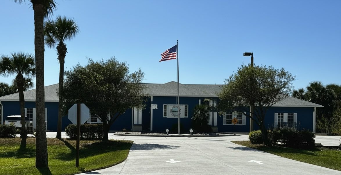 Blue building with an American flag and palm trees in front, viewed from a driveway under clear skies