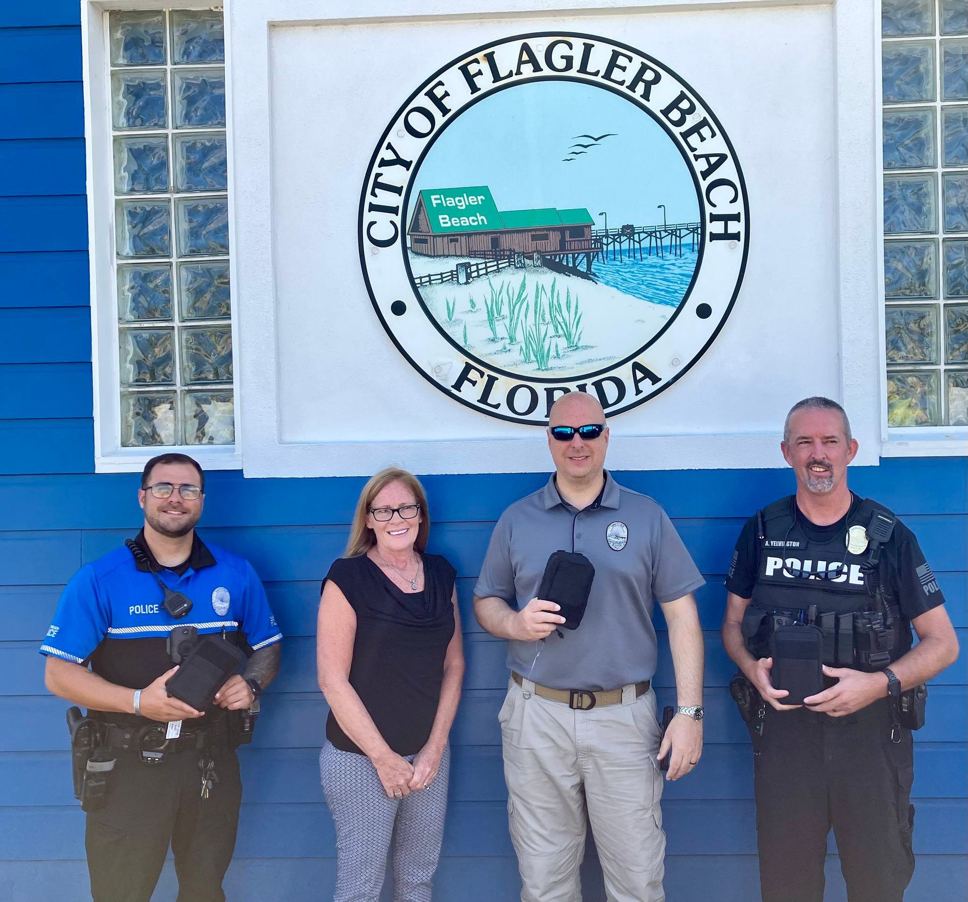 Four Flagler Beach police officers posing outside a city building under the Flagler Beach seal.