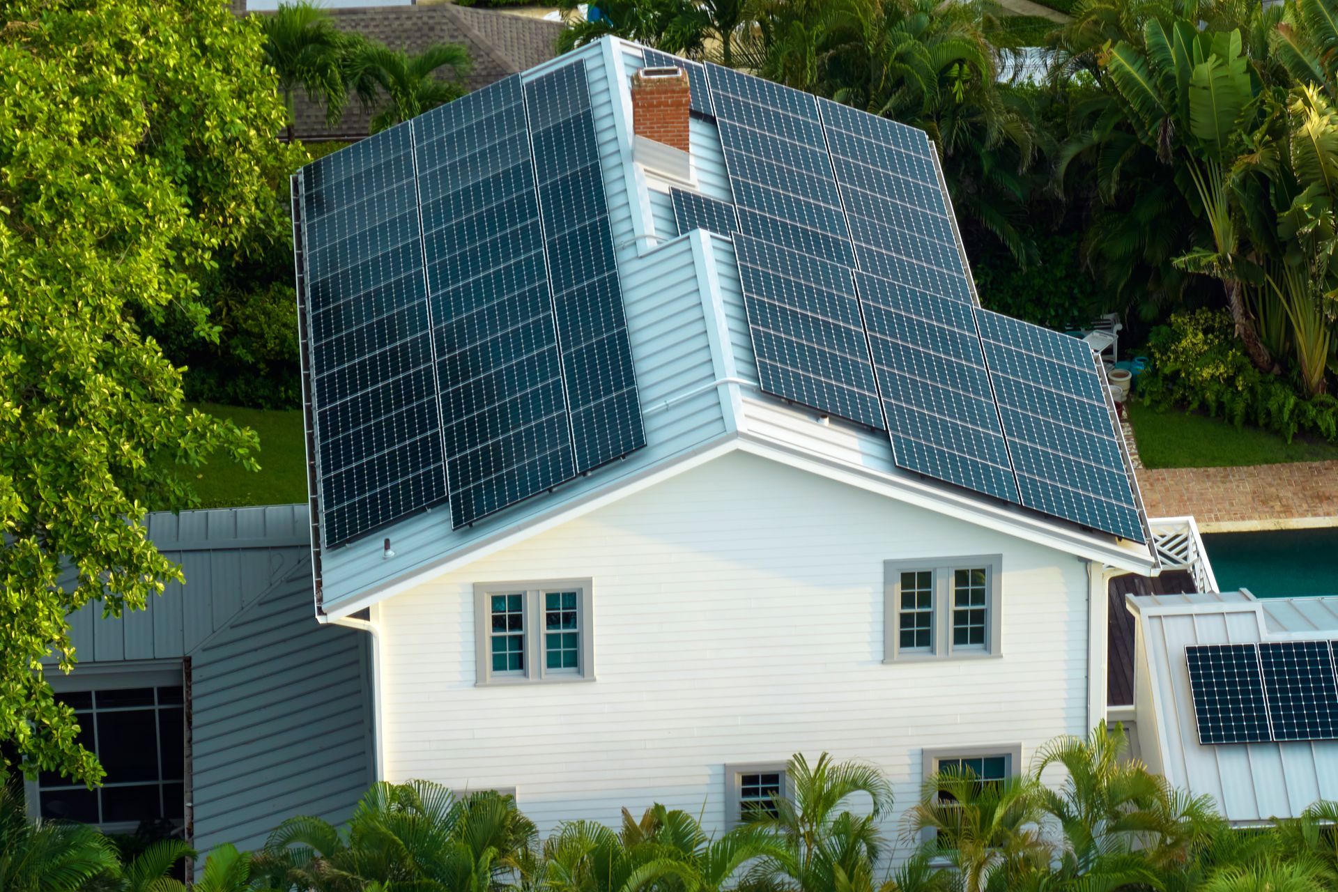 White house with solar panels on the roof, next to trees and a pool.