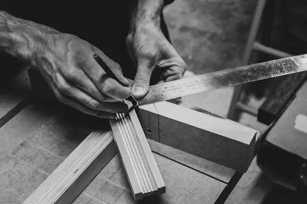 Mains d'artisan utilisant une équerre et un crayon pour le travail du bois.
