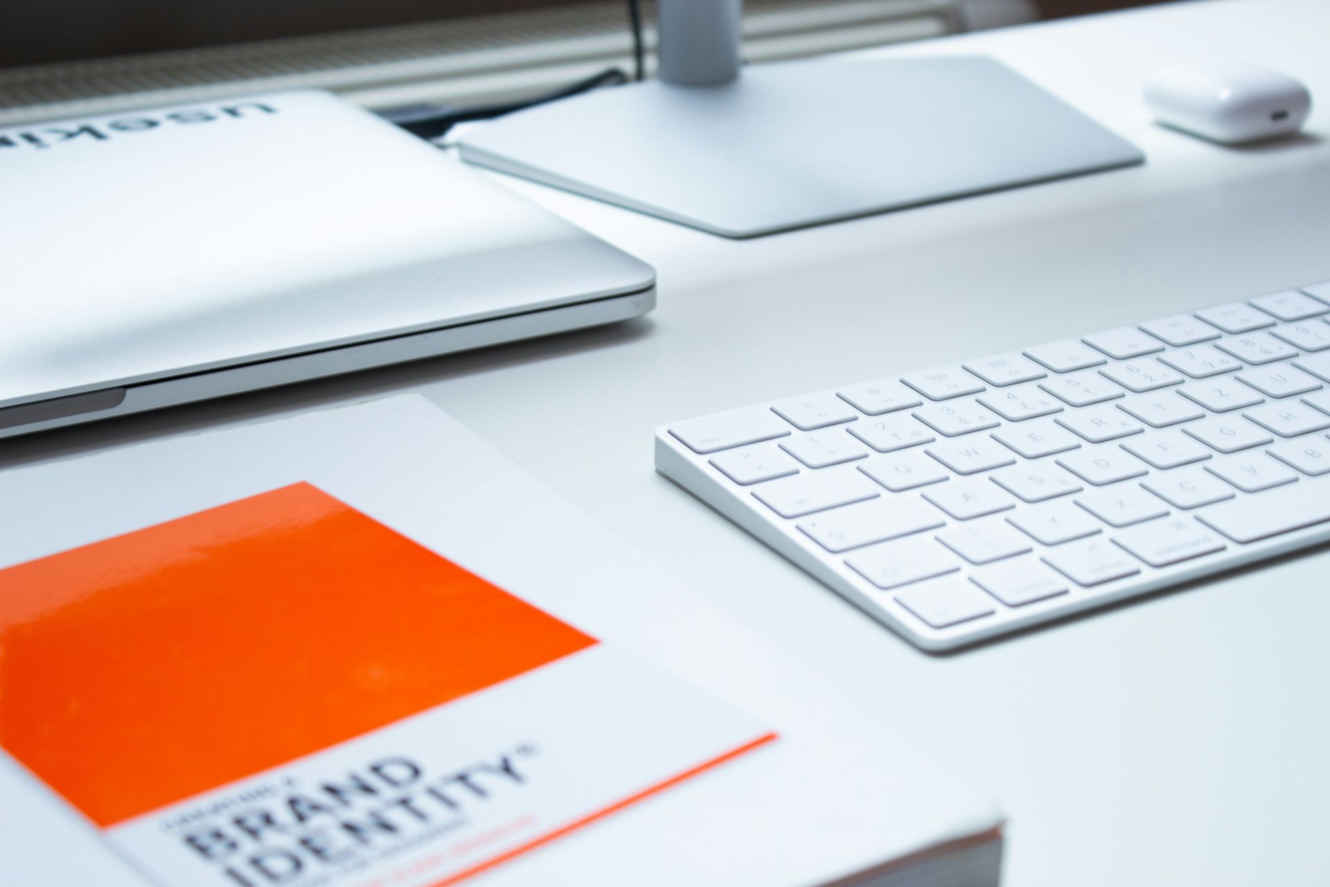 Ordinateur portable, clavier et un livre avec une couverture orange sur un bureau blanc.