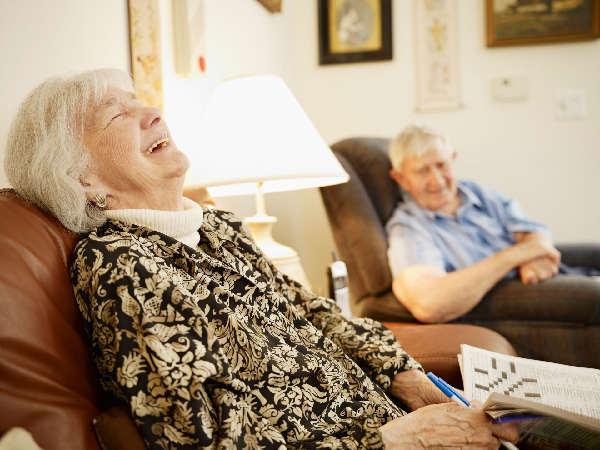 A happy elderly woman seated in a chair with her husband seated besides her.