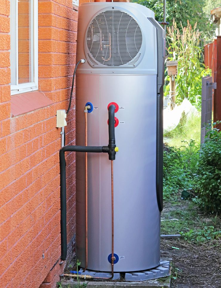 Outdoor gray water heater tank beside a brick wall, with pipes and greenery nearby — Hinch Plumbing In Breakwater, VIC