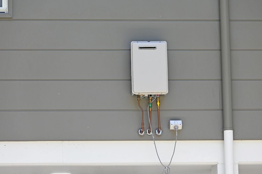Wall-mounted utility box with wires and a small outlet on a gray exterior wall — Hinch Plumbing In Breakwater, VIC