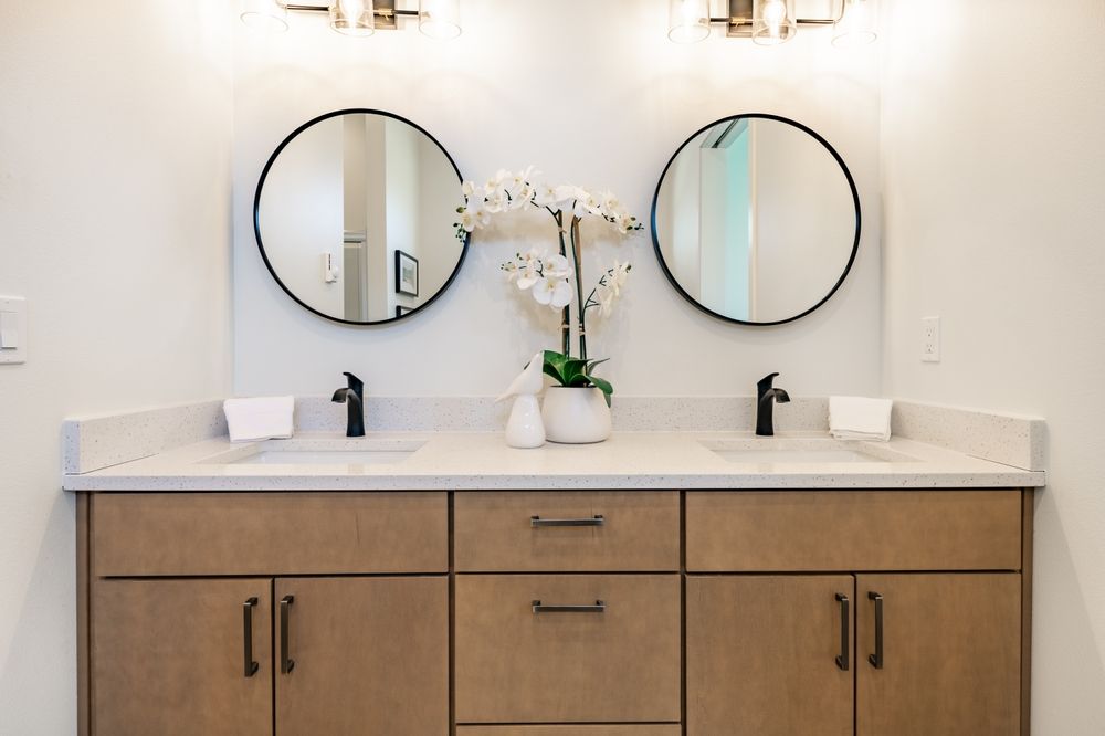 Modern bathroom vanity with double round mirrors, white countertop, and black faucets — Hinch Plumbing In Breakwater, VIC