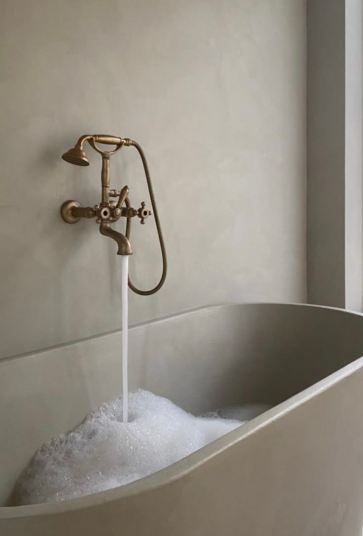 Vintage brass faucet filling a white bathtub with running water and bubbles — Hinch Plumbing In Breakwater, VIC