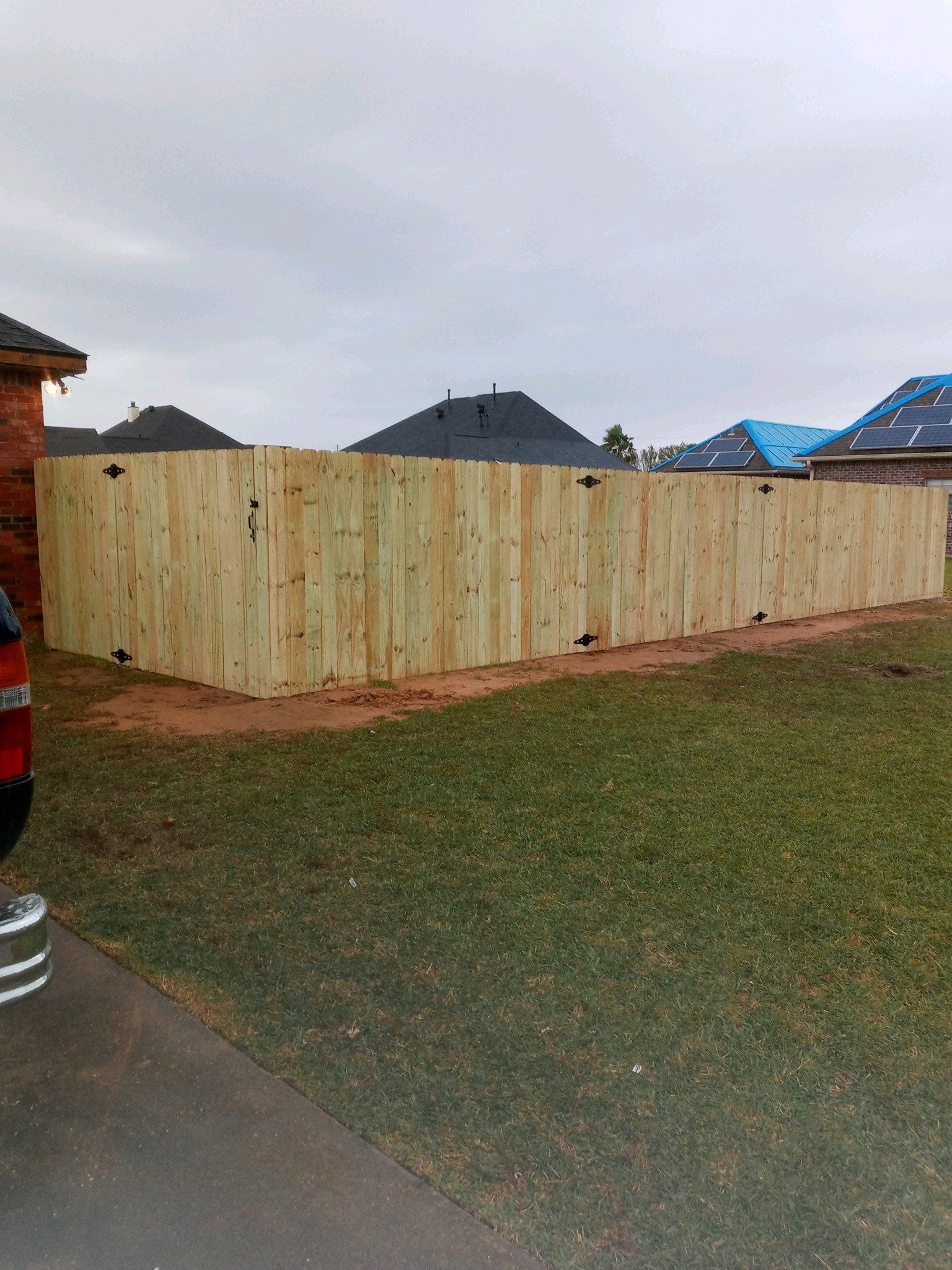 Wooden privacy fence along a grassy yard under a cloudy sky, with houses in the background.