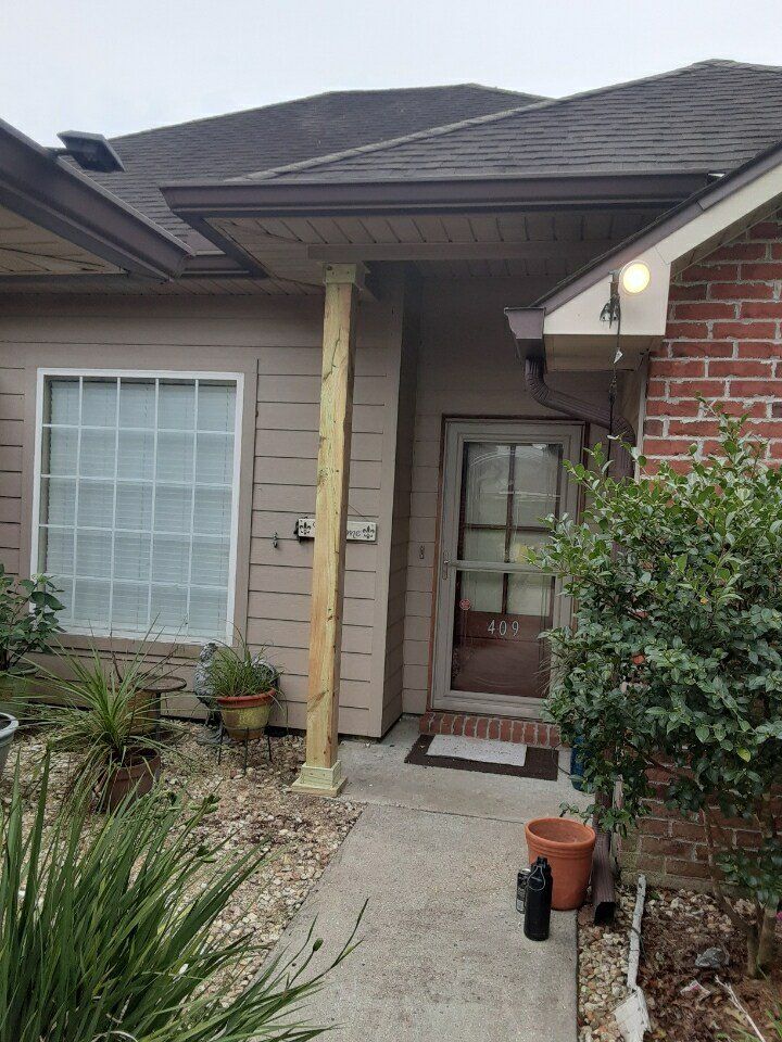 Front porch with beige siding, brick wall, glass door, windows, potted plants, and a single column。