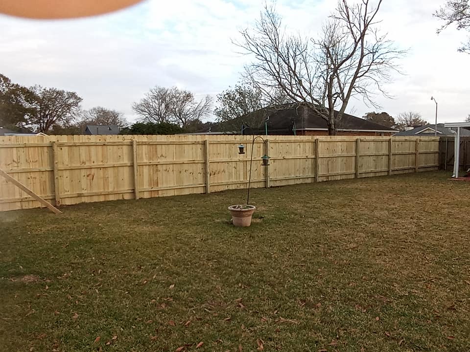 Backyard with a long wooden privacy fence and a small fire pit in the grass under an overcast sky