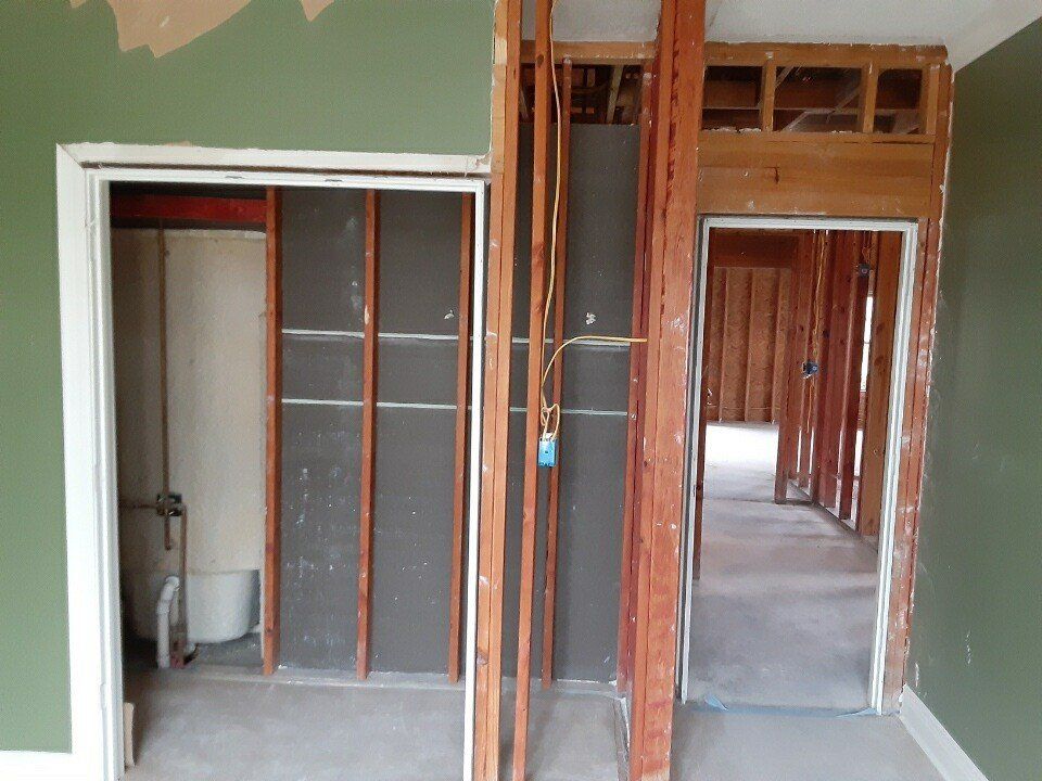 Interior of a house under renovation with exposed framing, open closets, and a doorway to a hall.