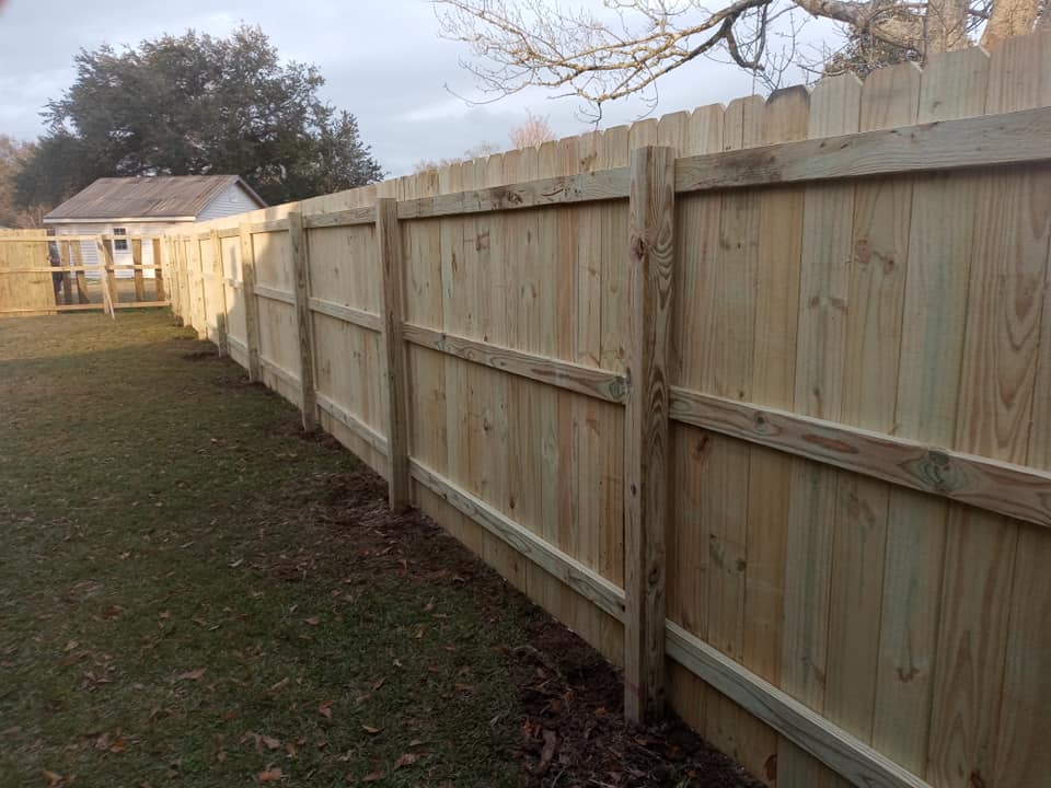 Long wooden privacy fence running along a grassy yard beside a small shed and trees
