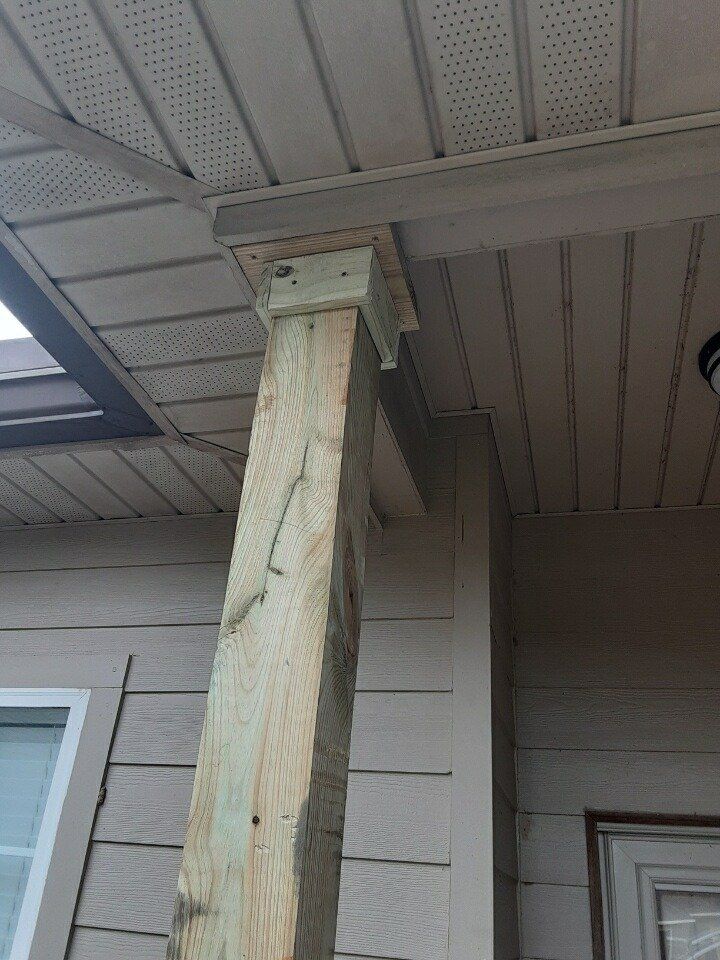 Close-up of a weathered wooden porch post supporting a roof overhang on a house.