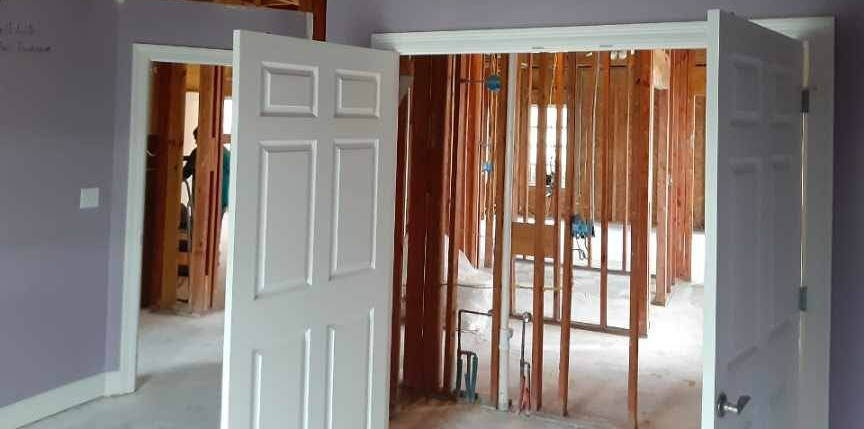 Interior room with open white doors and exposed wooden wall studs under renovation