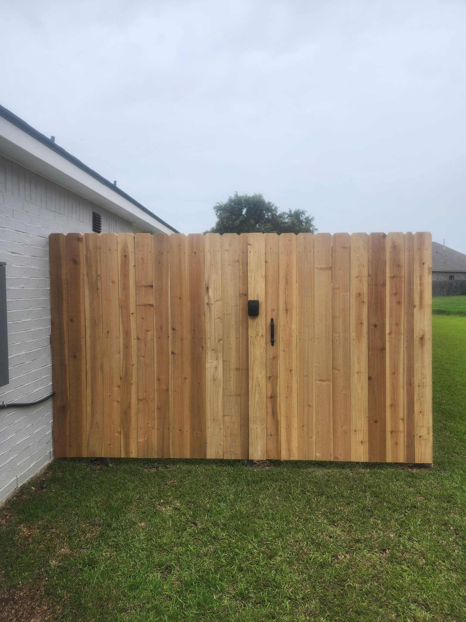 Wooden gate attached to a white house, opening onto a grassy yard under a cloudy sky