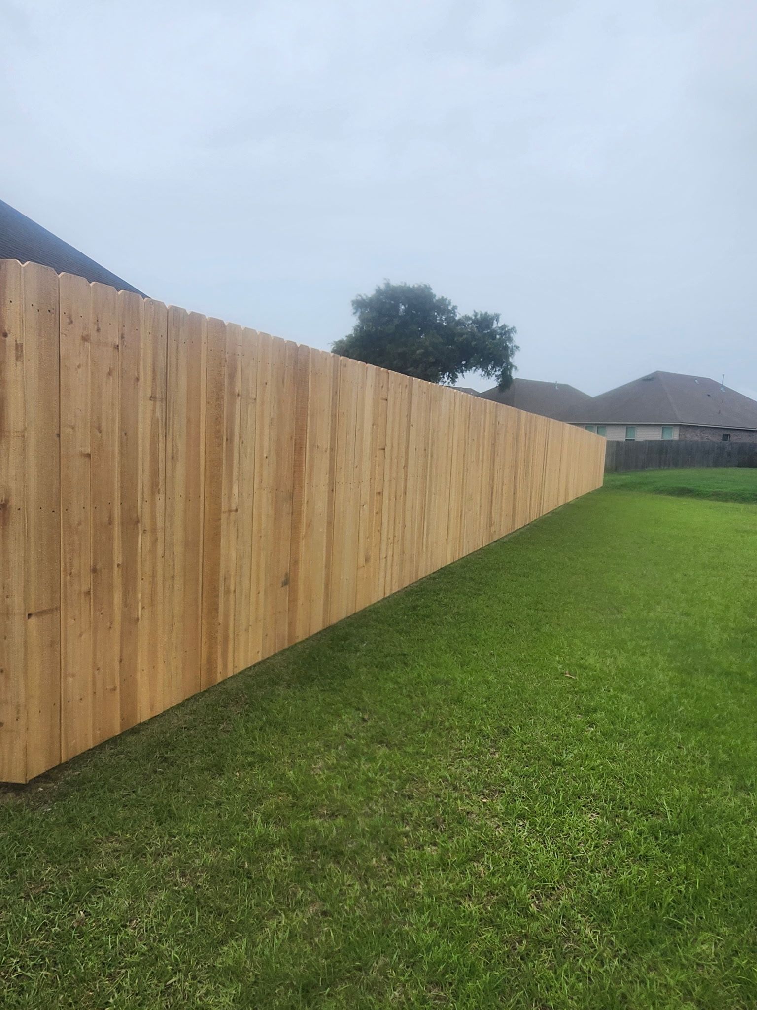 Fresh wooden fence along a green lawn under a cloudy sky, with houses in the distance