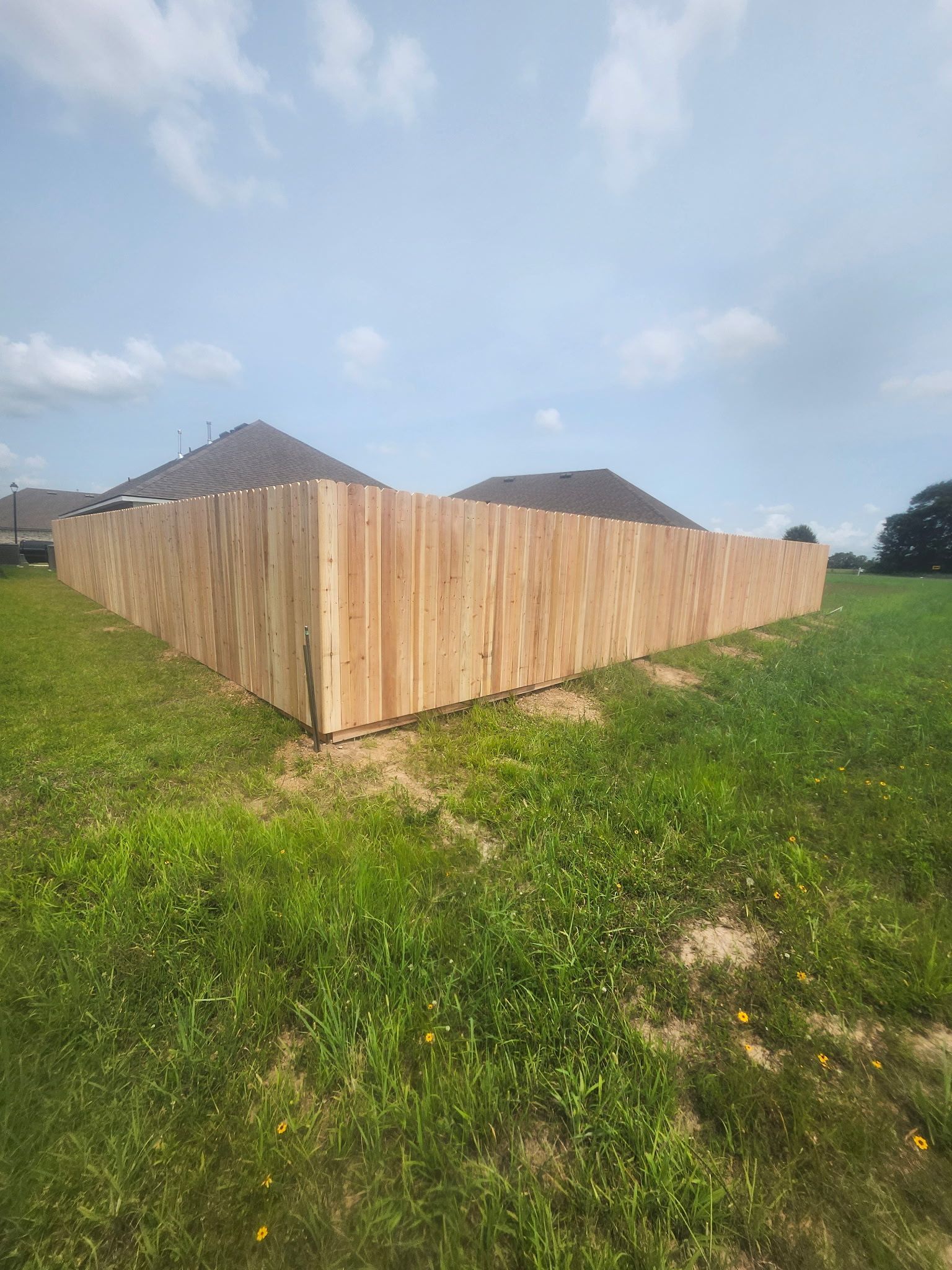 Wooden fence enclosing a grassy lot under a partly cloudy sky
