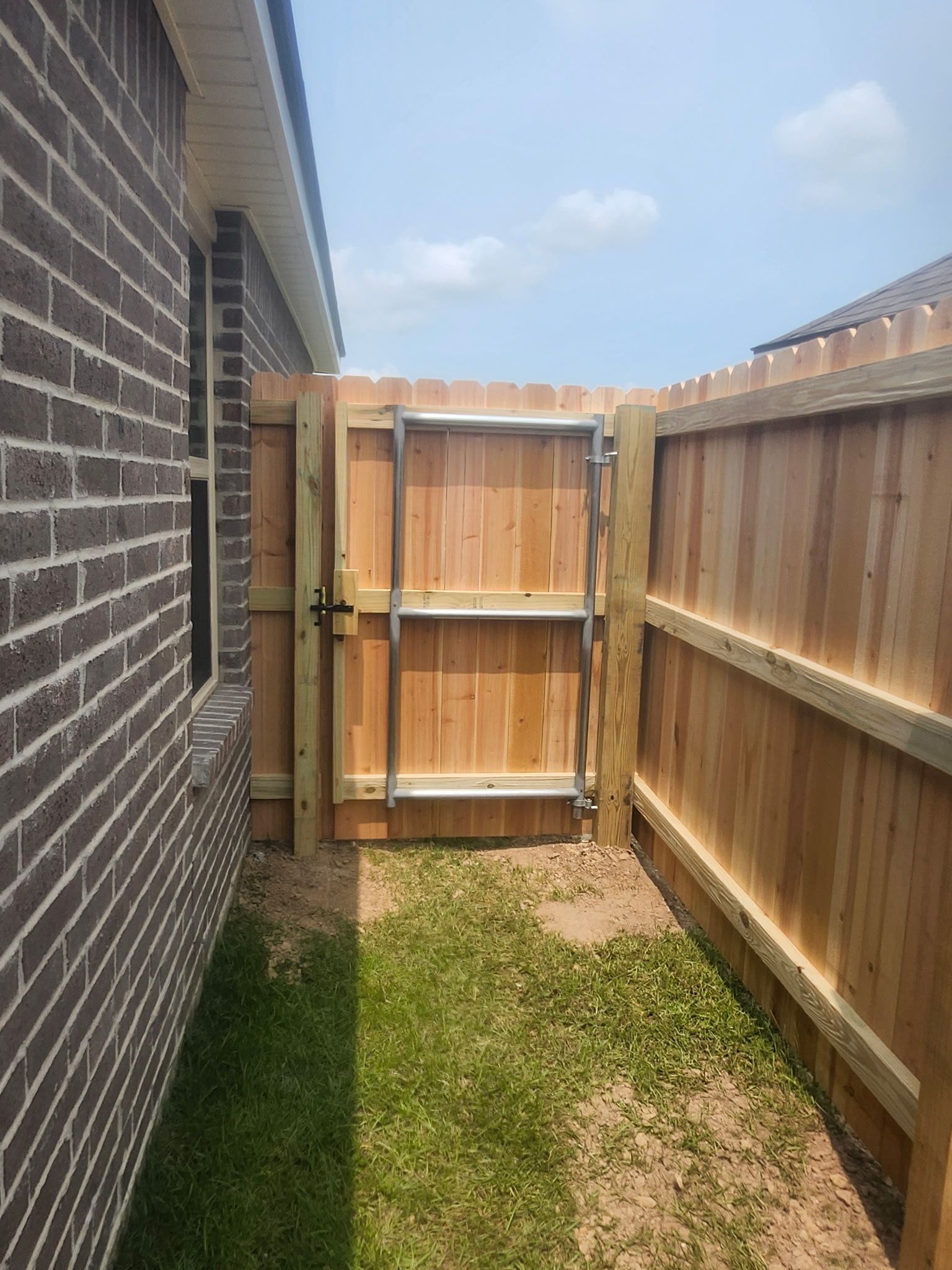 Narrow backyard side yard with brick wall, wooden fence, and a closed wooden gate on grass.