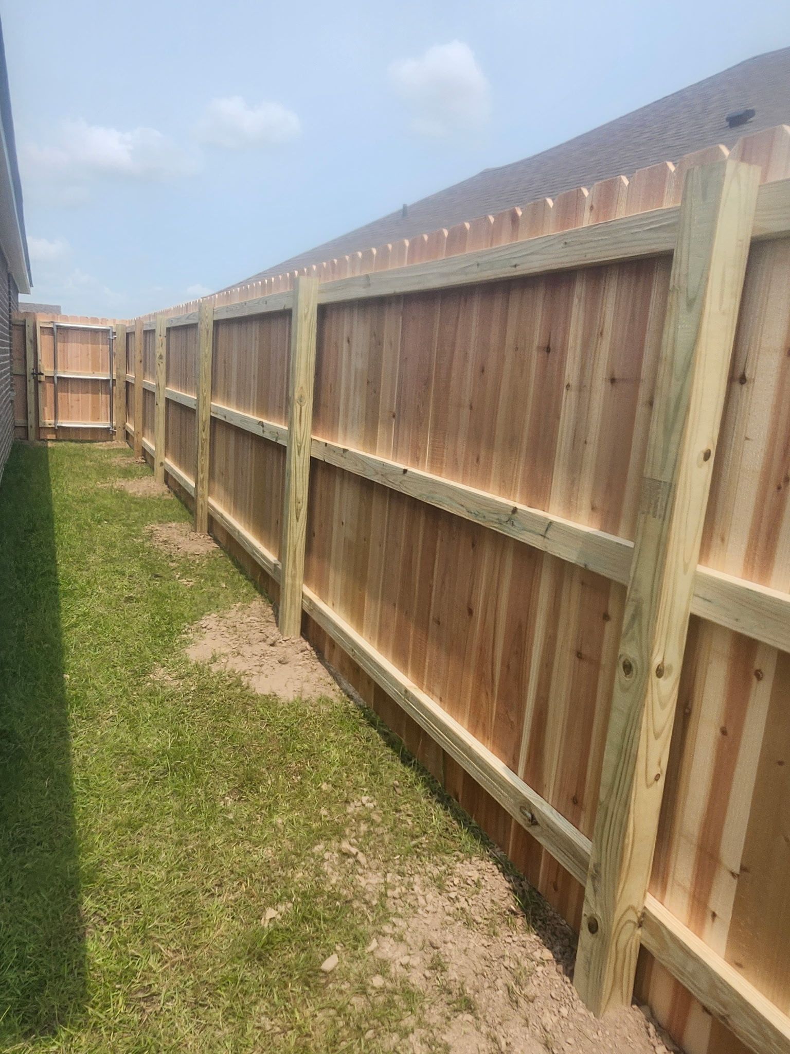 Wooden privacy fence along a narrow grassy side yard under a blue sky.