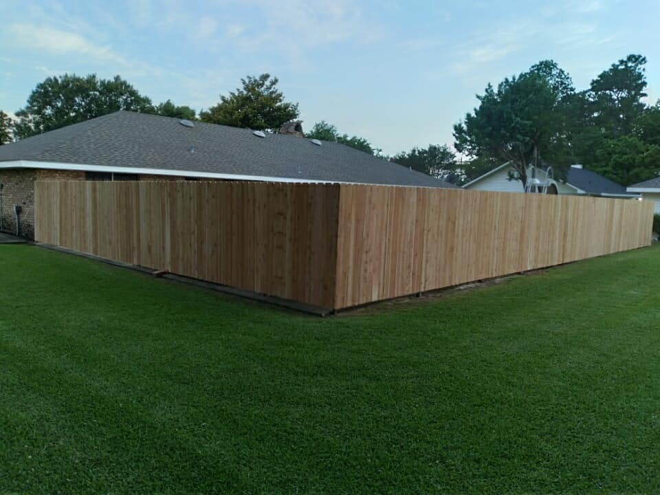Wooden privacy fence around a house on a green lawn at dusk
