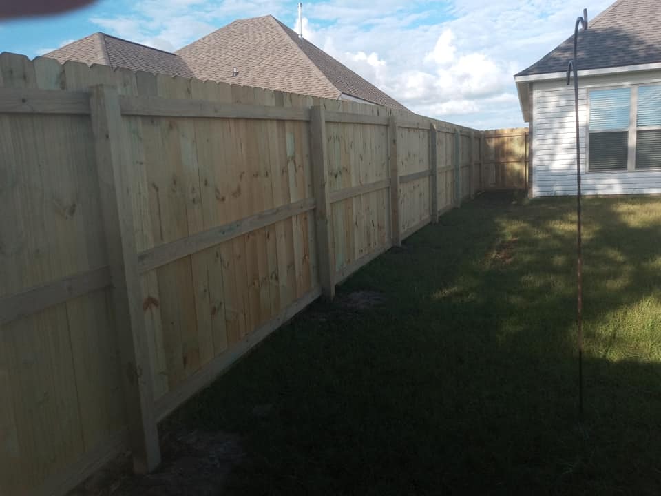 Wooden privacy fence along a grassy side yard beside a house under a partly cloudy sky
