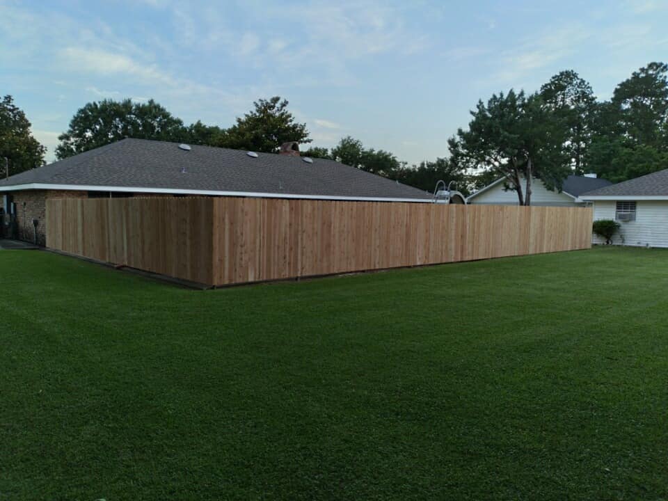 Single-story house with a wooden privacy fence in a grassy yard at dusk