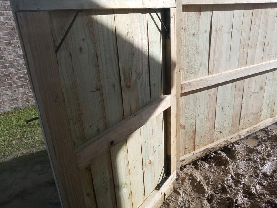 Wooden fence gate and panels along a dirt path, with a diagonal support brace.