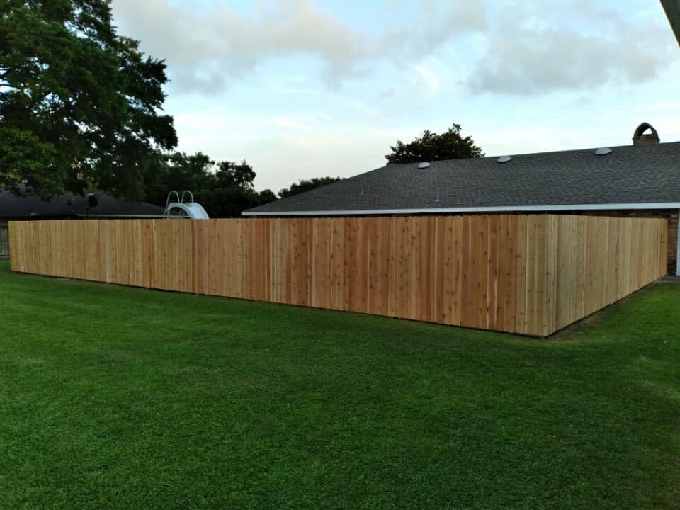 Long wooden fence around a grassy yard beside a house at dusk