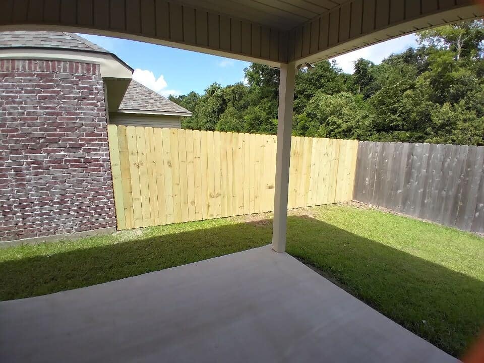 Covered patio overlooking a backyard with grass, a brick wall, and a wooden fence