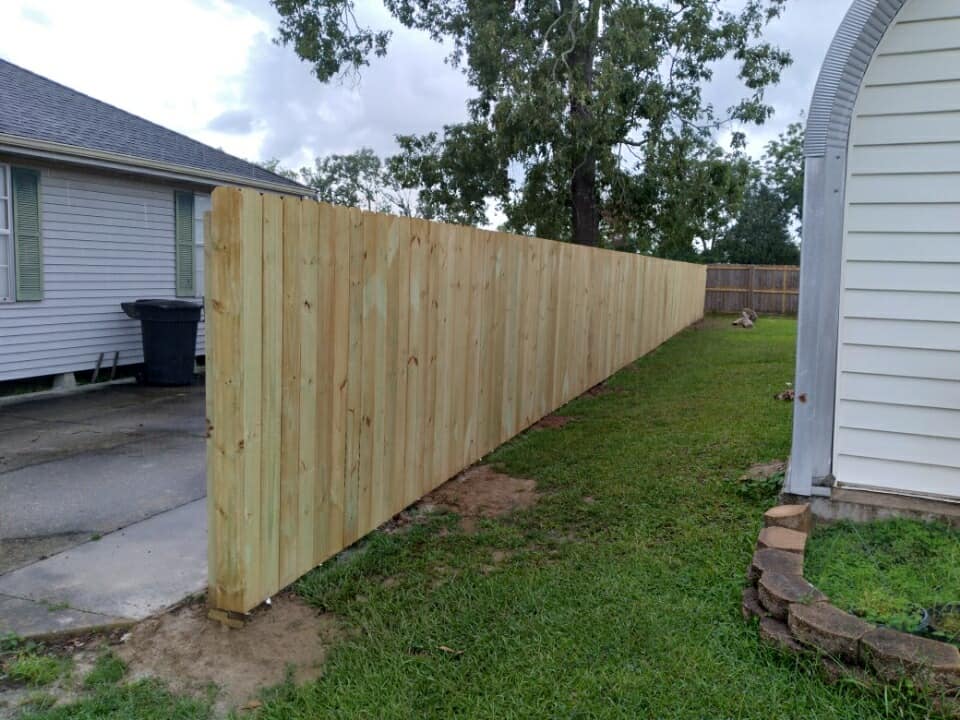 Freshly built wooden privacy fence along a narrow grassy side yard between two houses.