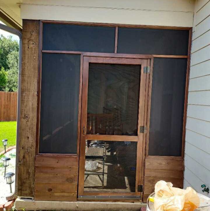 Screened porch door and windows on a house exterior, with wood paneling and construction materials nearby