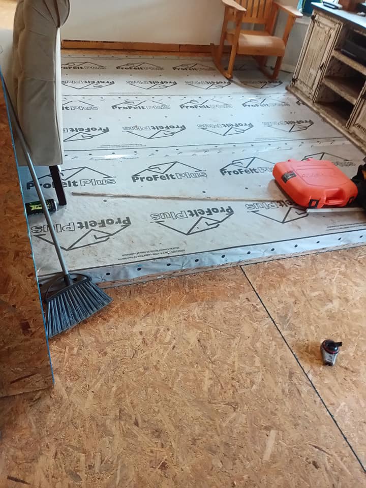 Partially installed flooring in a room, with underlayment, tools, and a red tool case on the floor.