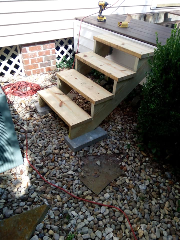 Wooden pet steps leading to a raised deck beside a brick house in a gravel yard.
