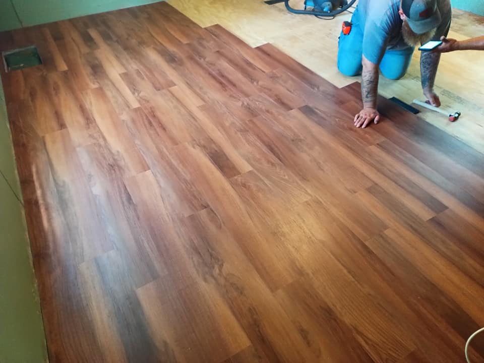 Worker installing wood flooring in a room, using a hand tool on brown planks.