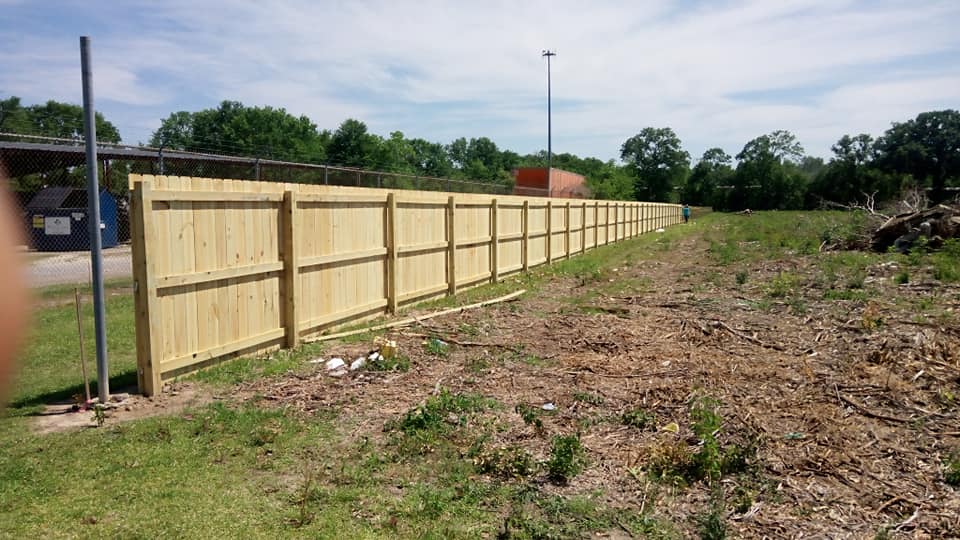 Freshly installed wooden fence along a grassy, partly cleared lot under a cloudy sky
