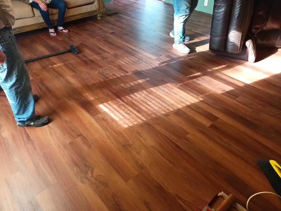 People’s legs and feet on a sunlit wooden floor in a room with chairs and furniture.