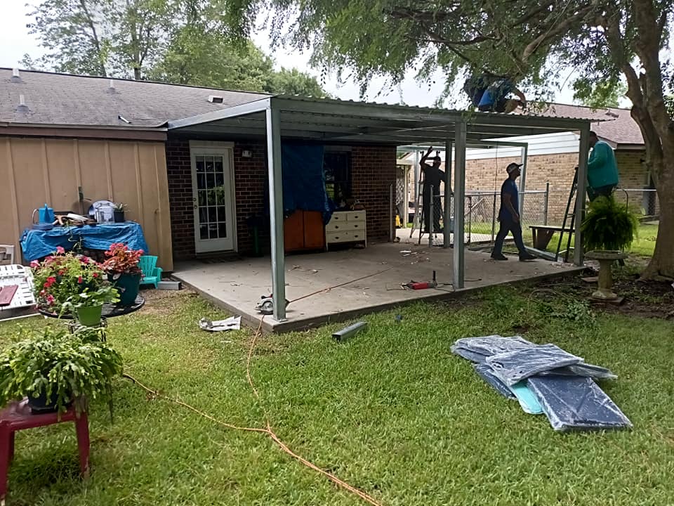 Backyard patio renovation with workers installing a covered deck beside a house