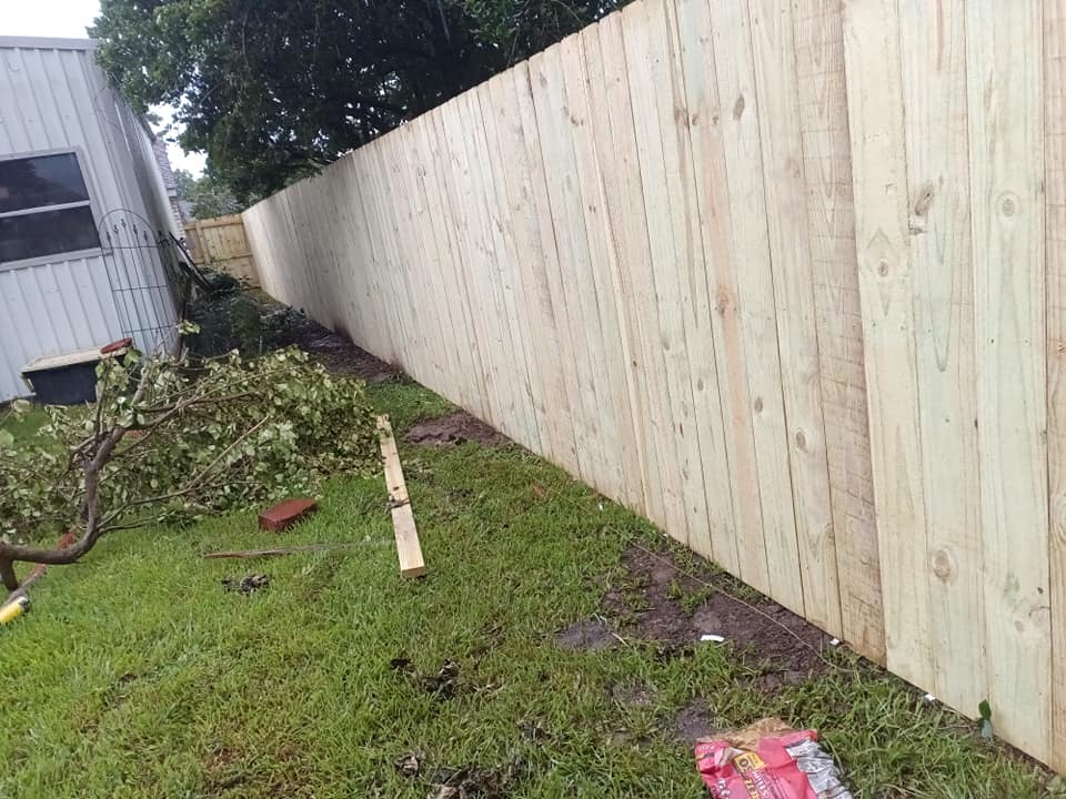 Long wooden fence along a grassy yard beside a building, with scattered debris and tree branches.