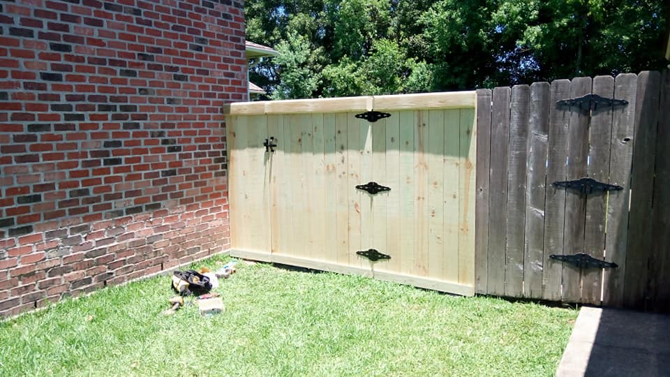 Backyard with brick wall, wooden fence, and a small dog lying on the grass.