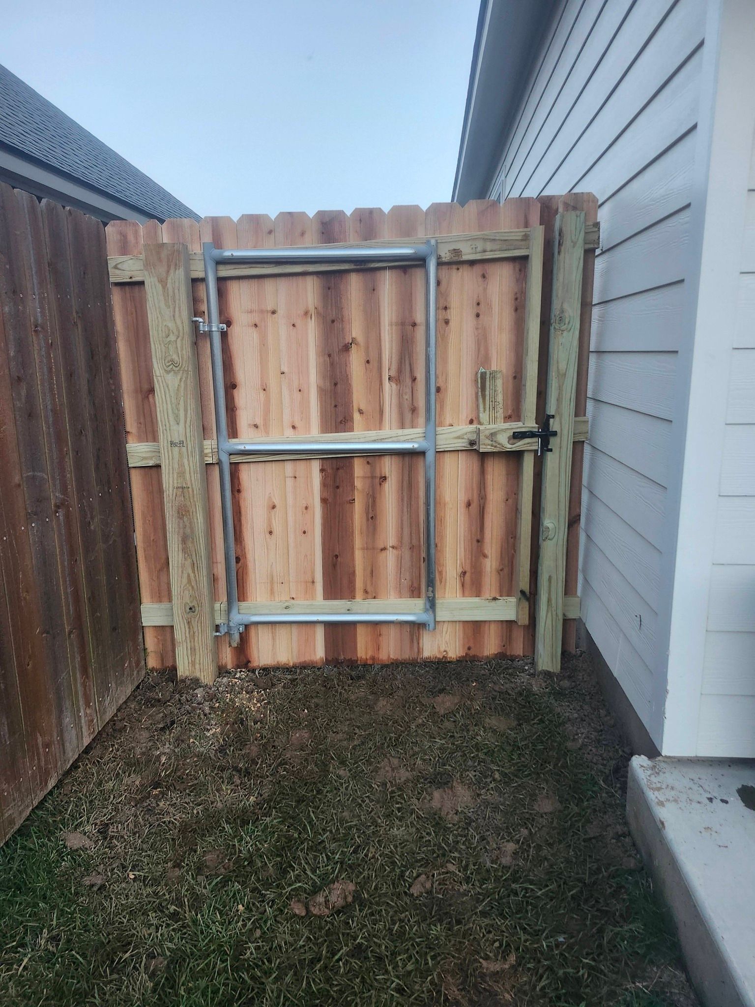 Wooden backyard gate between a brown fence and gray house siding, with grass below.