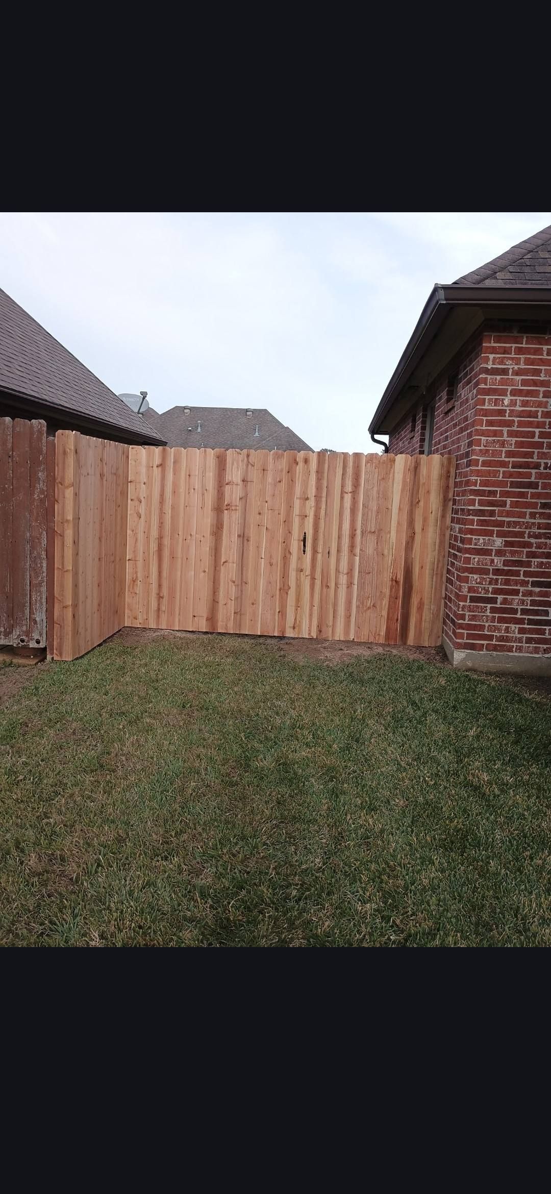 Wooden backyard fence between brick houses with grass in the foreground