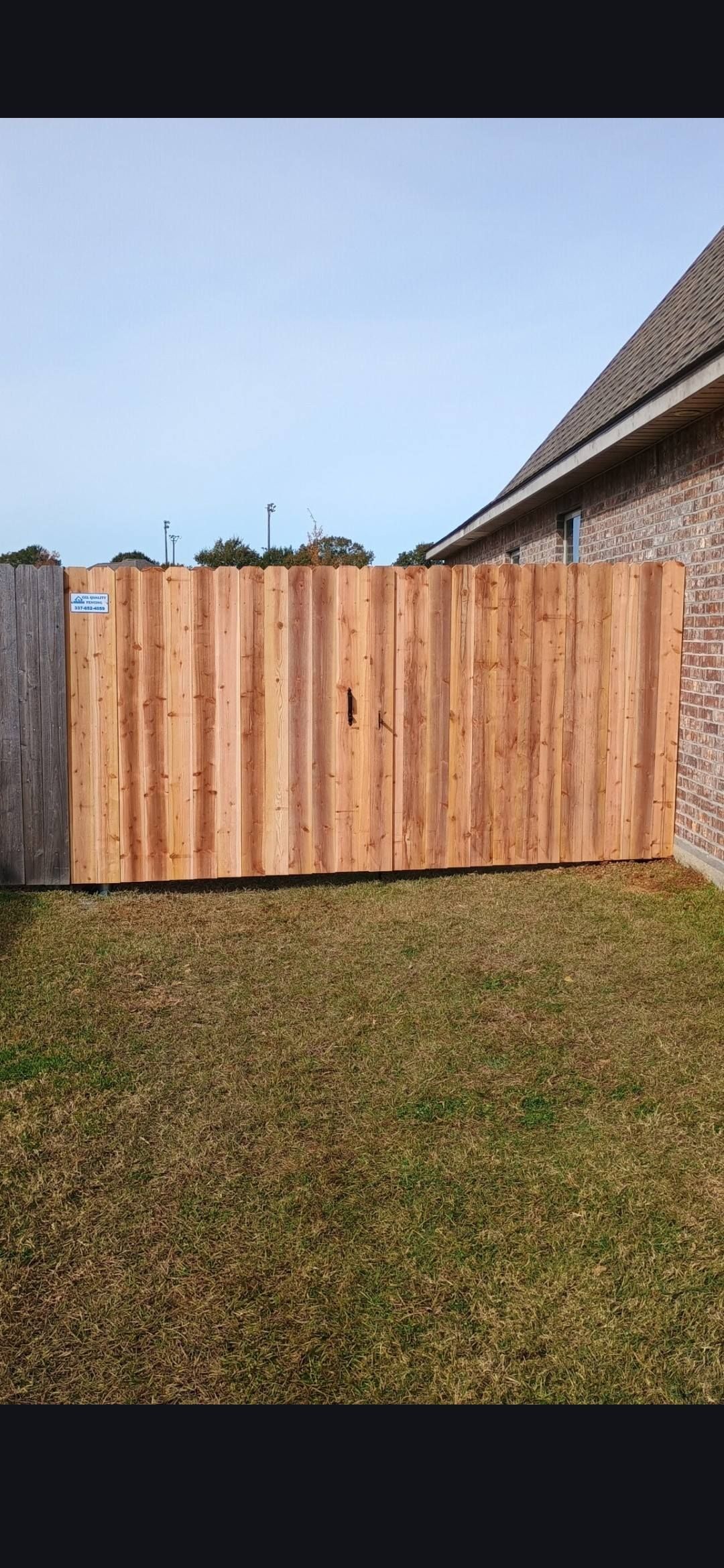 Wooden fence across a grassy backyard under a clear blue sky, with a thatched roof at right.