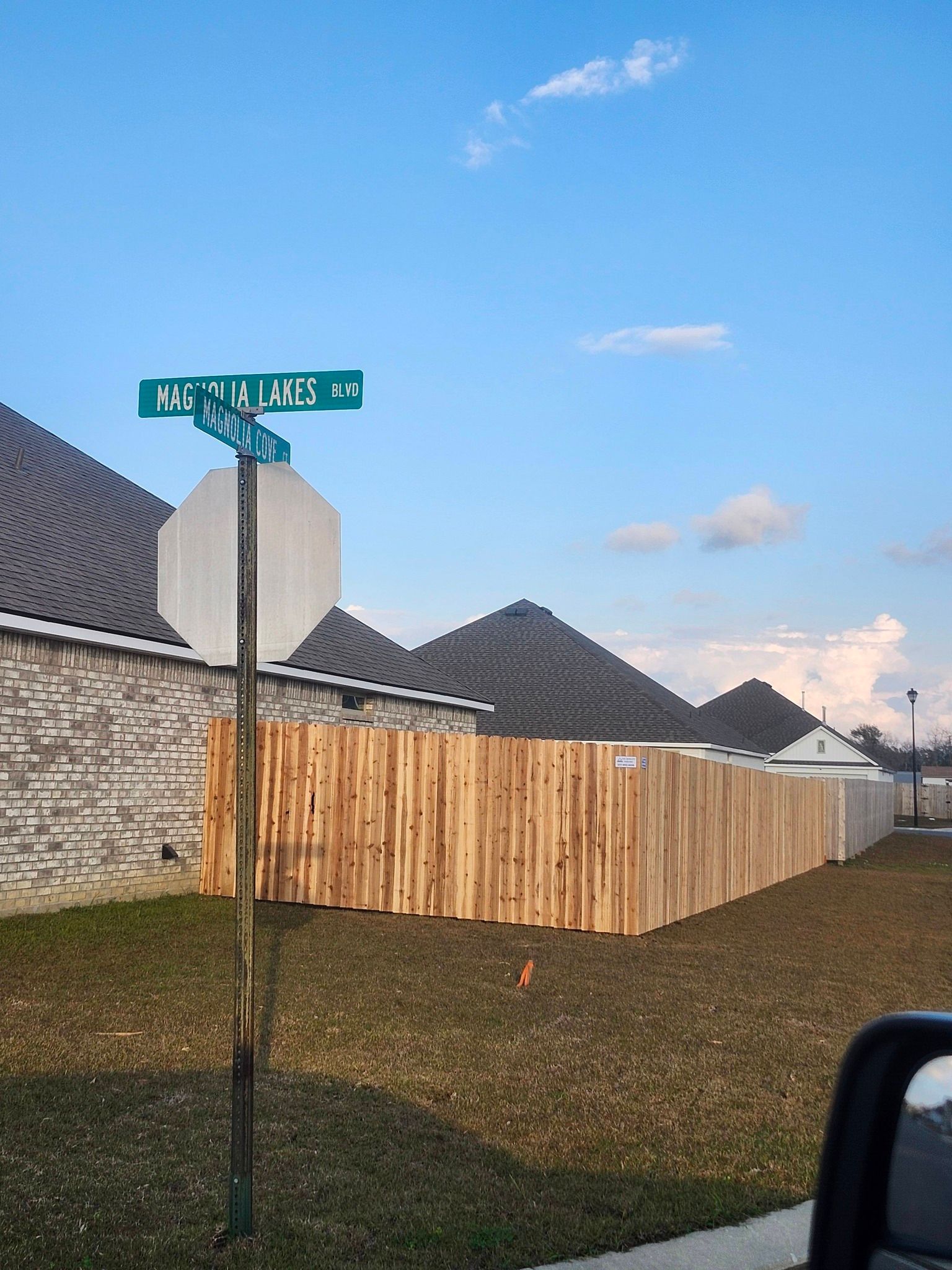 Street sign on a pole beside a wooden fence and suburban houses under a blue sky