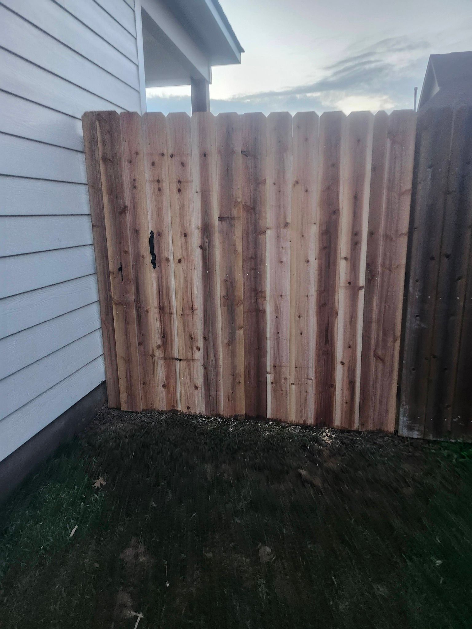 Weathered wooden fence beside a white house and patchy grass yard