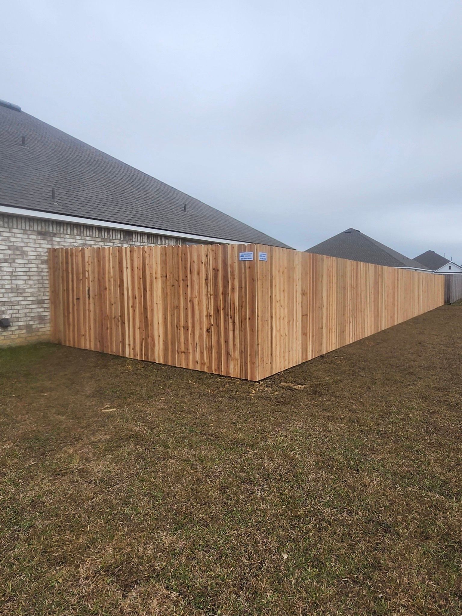Wooden privacy fence surrounding a yard beside a stone house under a cloudy sky